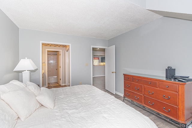 bedroom with a textured ceiling, dark wood-type flooring, and ensuite bath