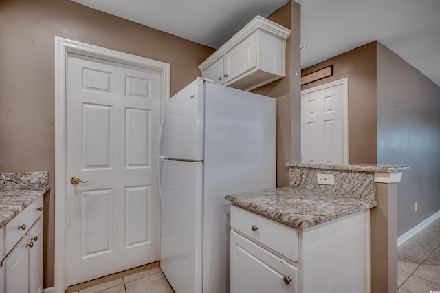 kitchen with white refrigerator, light tile patterned floors, light stone counters, and white cabinetry