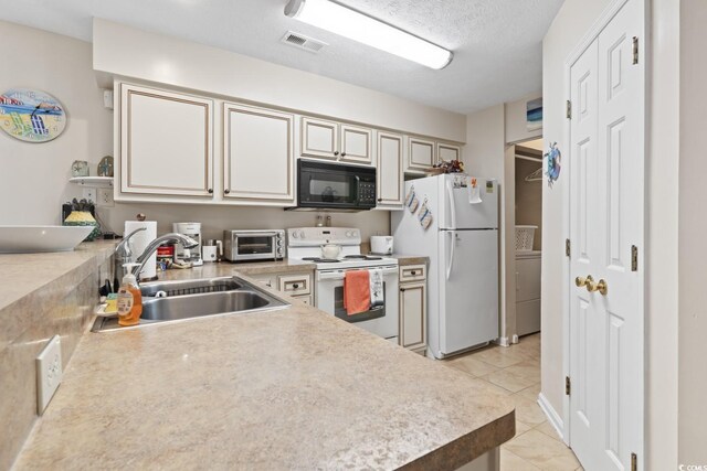 kitchen featuring a textured ceiling, light tile patterned flooring, sink, cream cabinetry, and white appliances