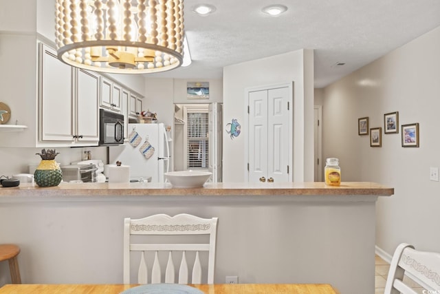 kitchen with black microwave, light countertops, a breakfast bar area, and freestanding refrigerator