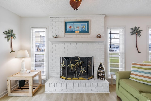 living room with a brick fireplace, a textured ceiling, light hardwood / wood-style flooring, and a healthy amount of sunlight