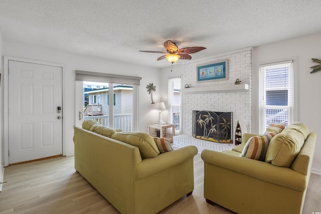 living room featuring light wood-type flooring, a textured ceiling, a fireplace, and ceiling fan