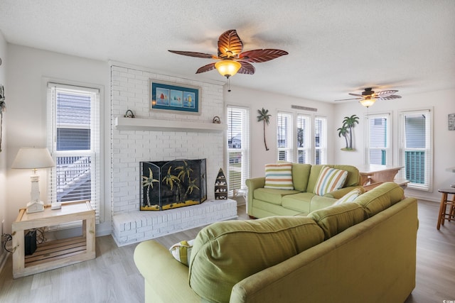 living room featuring ceiling fan, a textured ceiling, a fireplace, and light hardwood / wood-style floors