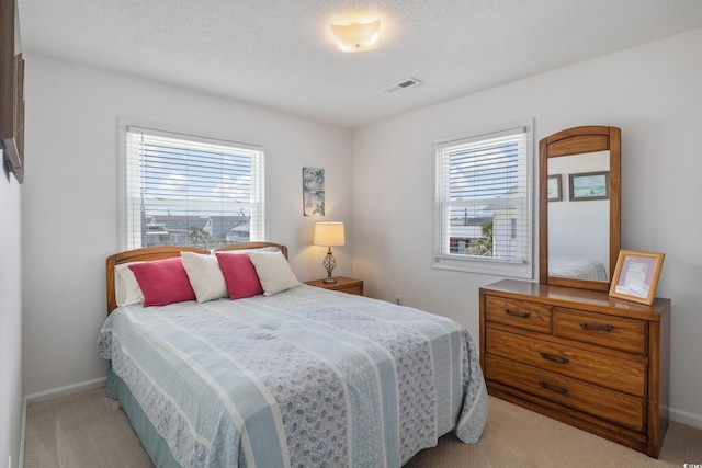 bedroom featuring multiple windows, a textured ceiling, and light carpet