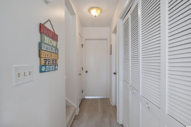 hall with a textured ceiling and light wood-type flooring