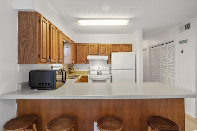 kitchen featuring a textured ceiling, a kitchen breakfast bar, kitchen peninsula, and white appliances