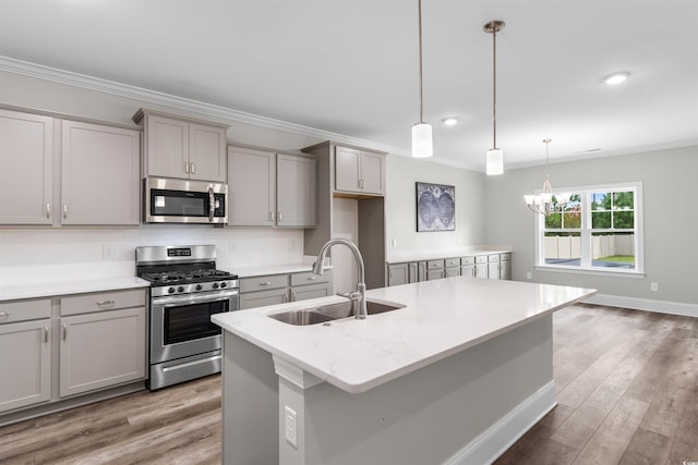 kitchen featuring pendant lighting, sink, a kitchen island with sink, stainless steel appliances, and light stone countertops