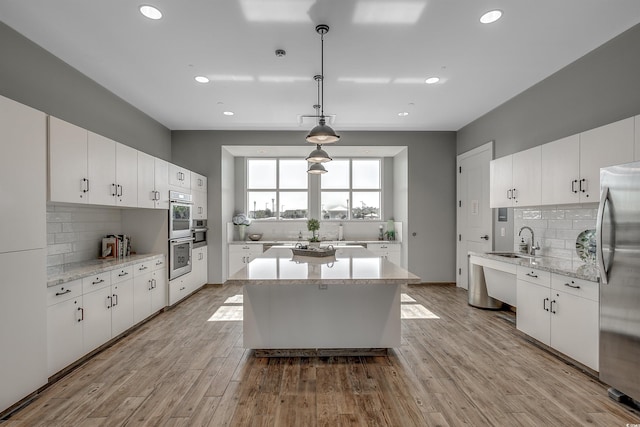 kitchen with stainless steel refrigerator, light hardwood / wood-style flooring, white cabinets, and decorative light fixtures