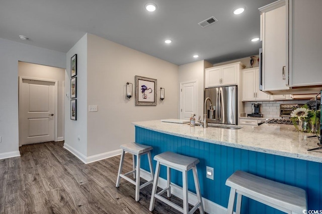 kitchen featuring kitchen peninsula, light hardwood / wood-style flooring, stainless steel fridge, a kitchen bar, and white cabinetry