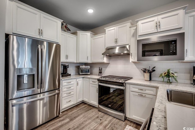 kitchen featuring appliances with stainless steel finishes, light wood-type flooring, tasteful backsplash, light stone counters, and white cabinets