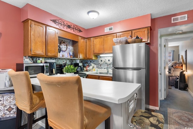 kitchen featuring a textured ceiling, backsplash, a kitchen bar, and stainless steel appliances