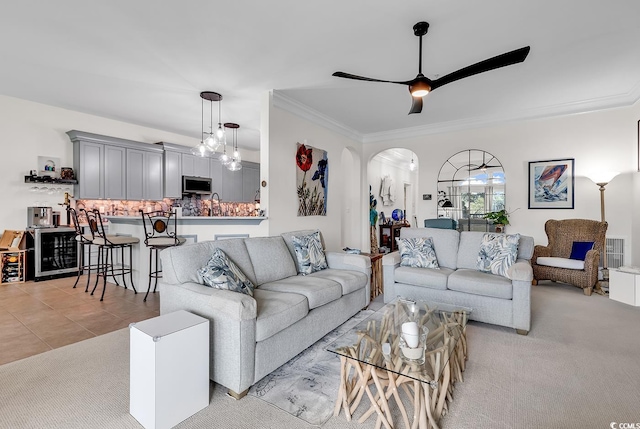 living room featuring ceiling fan, light colored carpet, ornamental molding, light tile patterned floors, and arched walkways