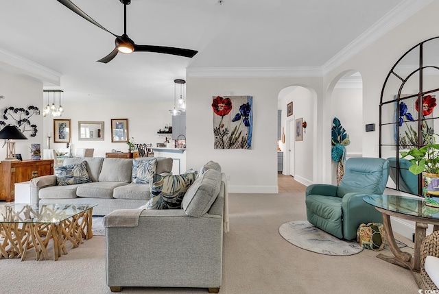 living area featuring baseboards, ornamental molding, light carpet, ceiling fan with notable chandelier, and arched walkways