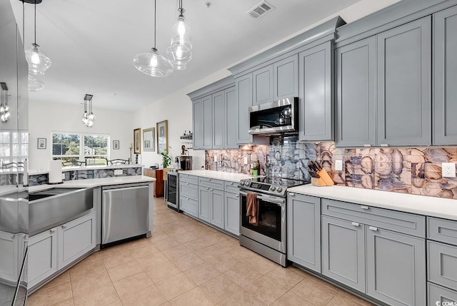 kitchen featuring visible vents, gray cabinetry, decorative backsplash, a sink, and stainless steel appliances