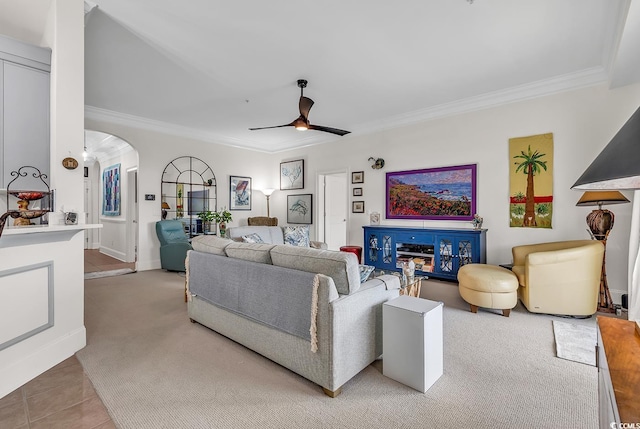 living room with tile patterned floors, carpet, ceiling fan, ornamental molding, and arched walkways