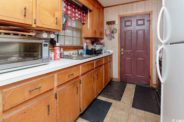 kitchen with white refrigerator, wood walls, sink, and crown molding