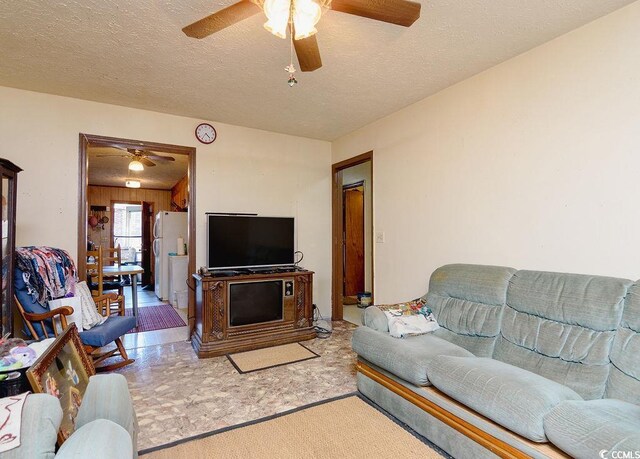 carpeted living room featuring ceiling fan, a textured ceiling, and wood walls