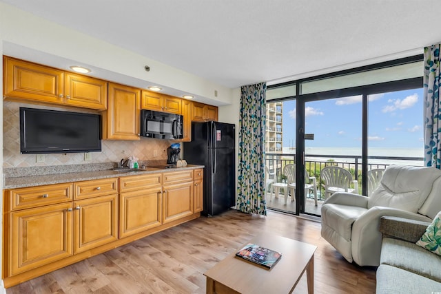 kitchen with light wood-type flooring, a wall of windows, light stone countertops, black appliances, and tasteful backsplash