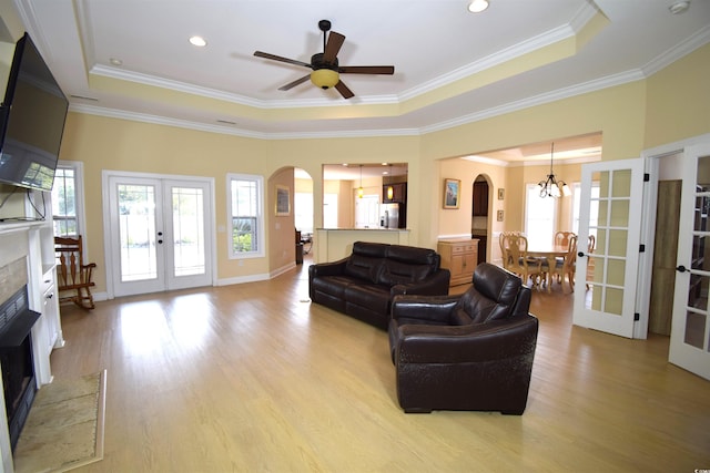 living room featuring french doors, ceiling fan with notable chandelier, a raised ceiling, and light hardwood / wood-style floors