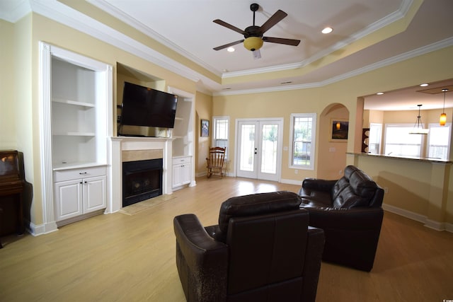 living room featuring light hardwood / wood-style floors, a tile fireplace, a tray ceiling, ceiling fan, and ornamental molding