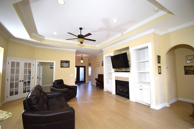 living room with french doors, light wood-type flooring, a raised ceiling, and ceiling fan