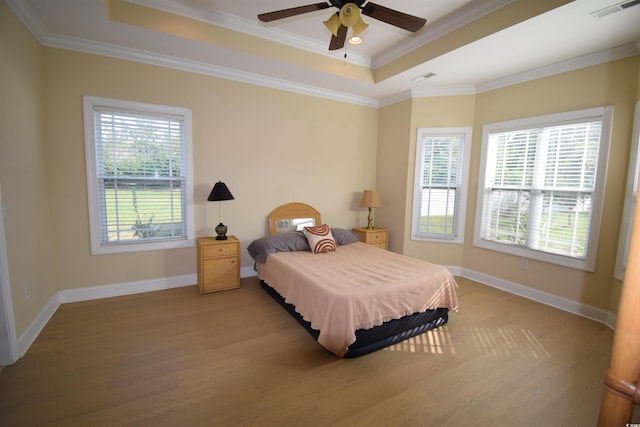 bedroom featuring wood-type flooring, a tray ceiling, ornamental molding, and ceiling fan