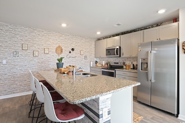 kitchen with a kitchen island with sink, appliances with stainless steel finishes, light stone countertops, and light hardwood / wood-style floors