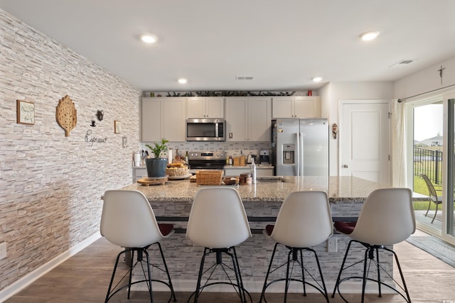 kitchen with dark hardwood / wood-style floors, a kitchen breakfast bar, appliances with stainless steel finishes, decorative backsplash, and light stone counters