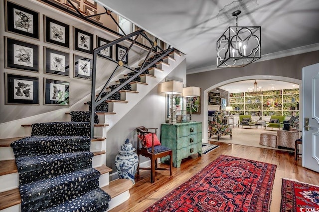 stairway with ornamental molding, a notable chandelier, and hardwood / wood-style floors