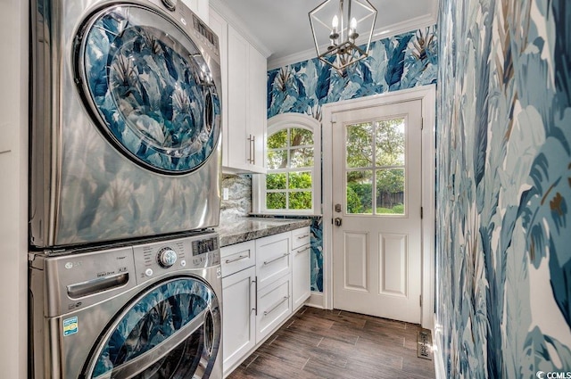 laundry area with cabinets, a notable chandelier, crown molding, stacked washer and clothes dryer, and dark hardwood / wood-style flooring