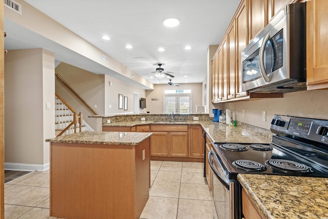 kitchen with black electric range oven, sink, light stone counters, a center island, and light tile patterned floors