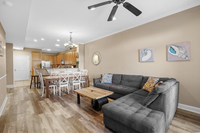 living room featuring crown molding, ceiling fan with notable chandelier, and light hardwood / wood-style flooring