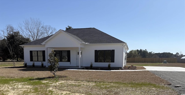 modern farmhouse featuring a shingled roof and fence