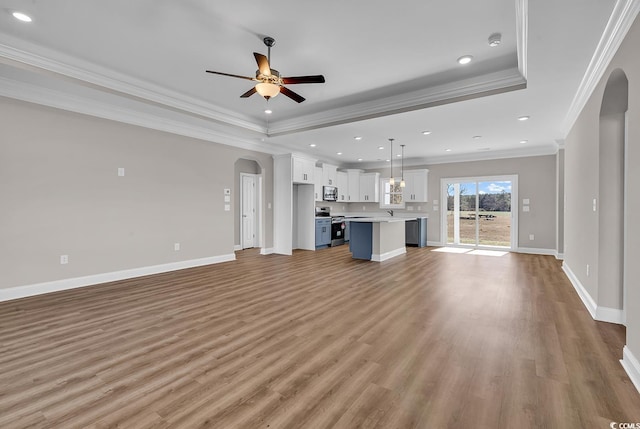 unfurnished living room featuring a raised ceiling, light wood-style flooring, baseboards, and arched walkways