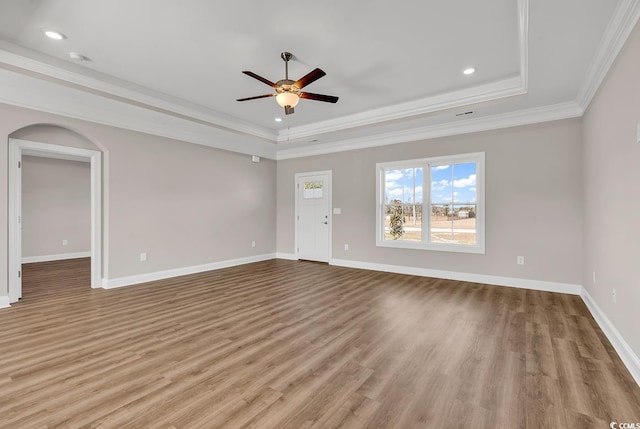 unfurnished living room featuring a raised ceiling, wood finished floors, baseboards, and ornamental molding