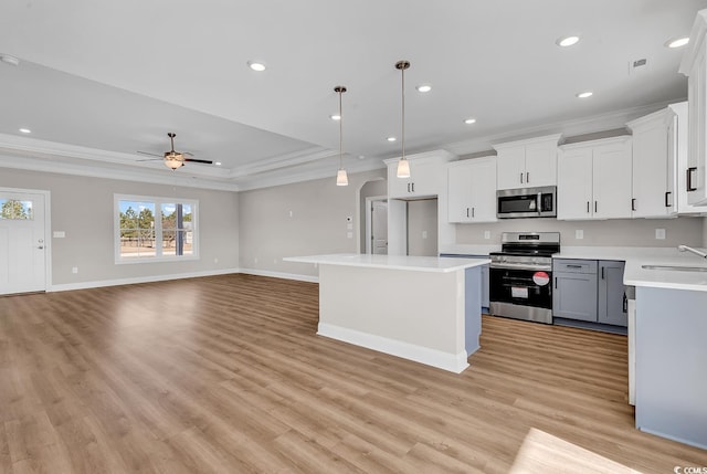 kitchen featuring light wood-style flooring, ornamental molding, a sink, appliances with stainless steel finishes, and light countertops