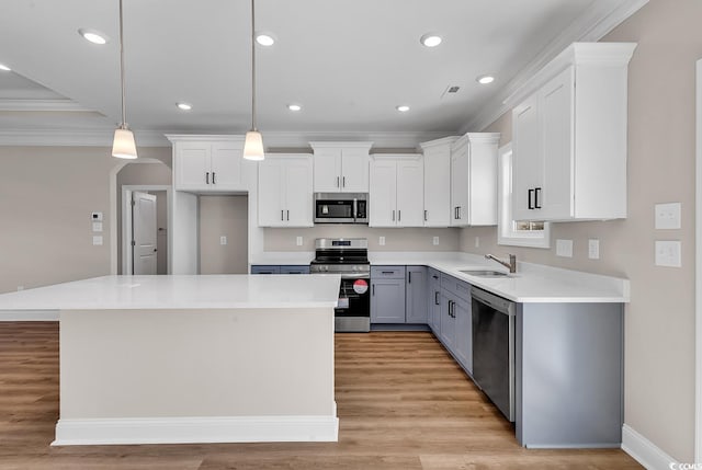 kitchen with a center island, ornamental molding, appliances with stainless steel finishes, white cabinets, and a sink