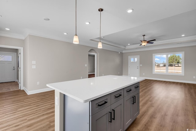 kitchen featuring light wood finished floors, gray cabinetry, light countertops, ornamental molding, and arched walkways