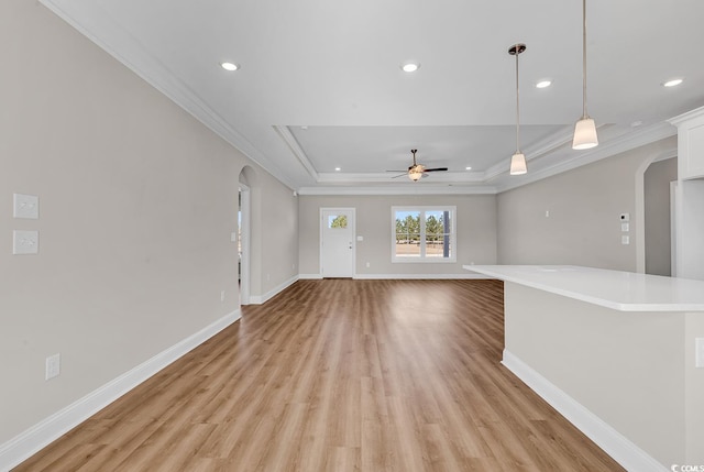 unfurnished living room with a raised ceiling, ornamental molding, arched walkways, light wood finished floors, and baseboards