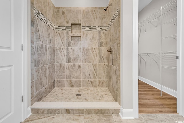 full bathroom featuring a walk in closet, tiled shower, and baseboards