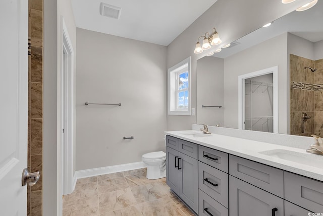 bathroom featuring a sink, tiled shower, toilet, and double vanity