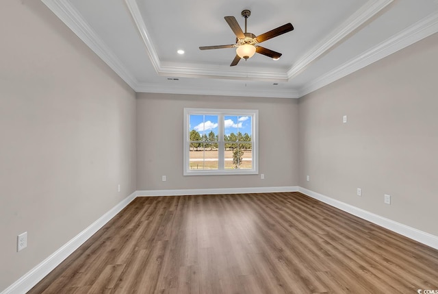 empty room with crown molding, ceiling fan, baseboards, wood finished floors, and a raised ceiling