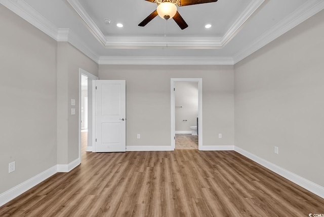 unfurnished bedroom with a tray ceiling, wood finished floors, and baseboards