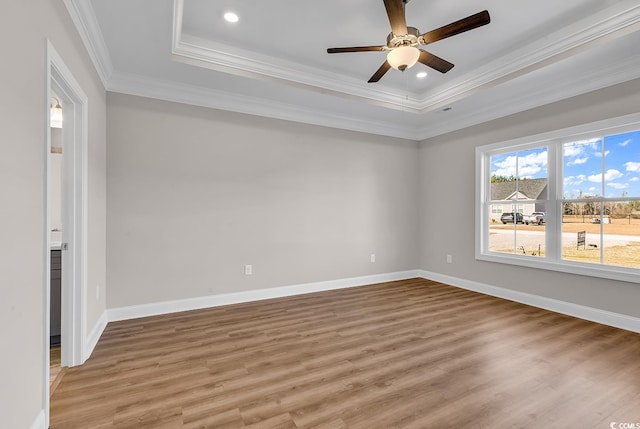 unfurnished room featuring a raised ceiling, light wood-style flooring, crown molding, and baseboards