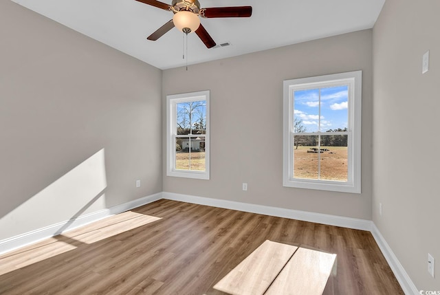 spare room featuring a wealth of natural light, visible vents, baseboards, and wood finished floors