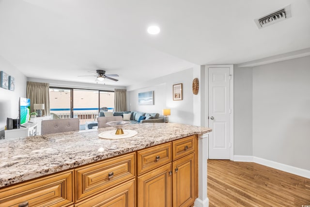 kitchen featuring light stone counters, ceiling fan, and light hardwood / wood-style floors