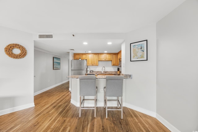 kitchen with light wood-type flooring, stainless steel refrigerator, kitchen peninsula, a kitchen breakfast bar, and decorative backsplash