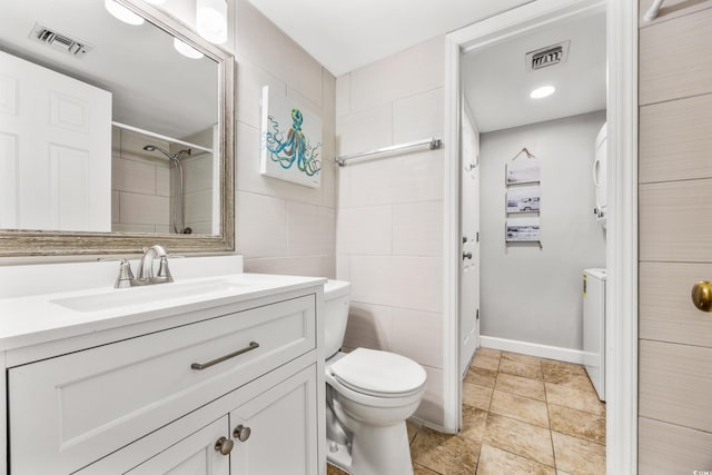 bathroom featuring toilet, a shower, tile walls, washing machine and clothes dryer, and vanity