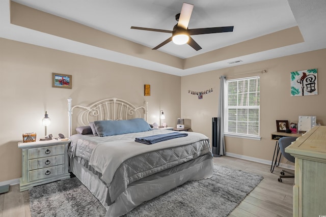 bedroom featuring a tray ceiling, ceiling fan, and light hardwood / wood-style flooring