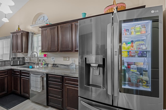 kitchen with vaulted ceiling, stainless steel appliances, sink, light stone counters, and dark brown cabinetry